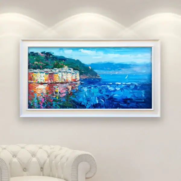 An original Portofino oil painting with a sleek white frame displayed in a bright modern interior, showing the colorful Mediterranean houses against a clean wall.
