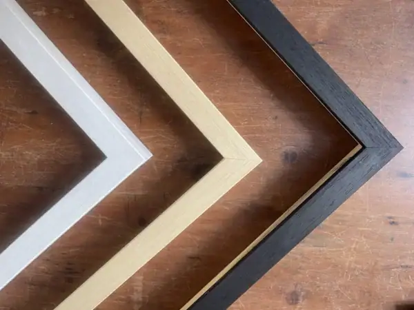 Corner view of wooden frames in natural wood, white, and black finishes, highlighting the shape, thickness, and craftsmanship of each frame