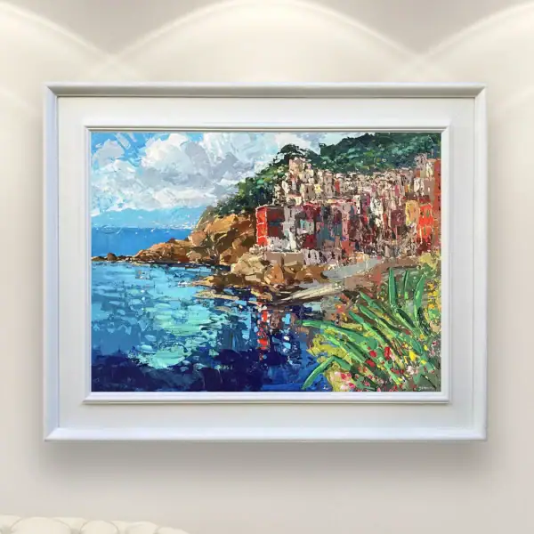 Original horizontal oil painting of Riomaggiore by Agostino Veroni, displayed in a white frame on a gallery wall next to a classic white armchair.