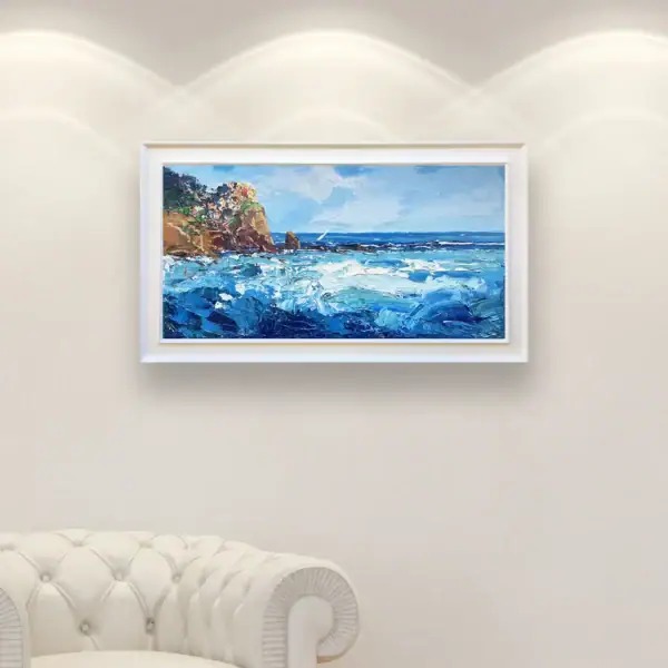 The original Manarola oil painting in a white frame, displayed in a bright, modern interior next to a classic white armchair.
