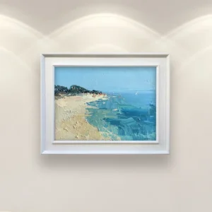 Beach oil painting on canvas on a light-colored wall above a sofa, framed horizontal artwork showing a serene coastal shoreline with calm sea and sandy beach