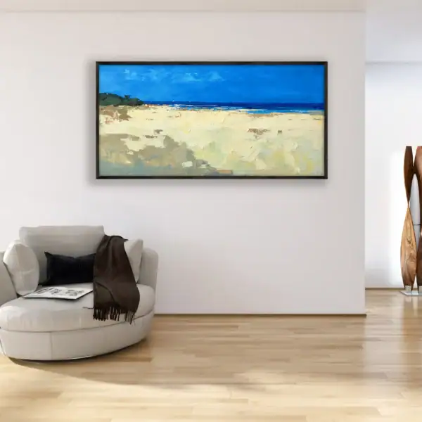 A large horizontal contemporary impressionist beach painting hanging in a bright, modern living room next to a white armchair.