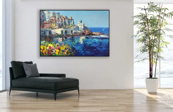 The horizontal Amalfi coast seascape canvas styled in a modern black frame as a vibrant focal point on a white wall in a luxury contemporary lounge room next to a potted tree.
