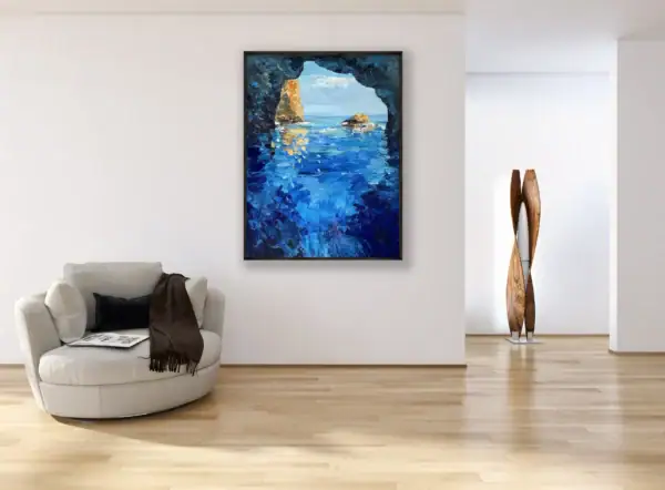 The vertical Blue Grotto oil painting displayed as an elegant coastal focal point in a bright contemporary room near a modern grey armchair.