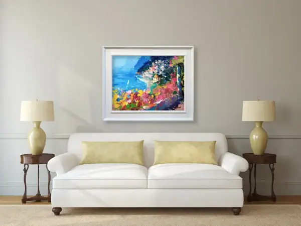The horizontal Positano seascape canvas displayed in a white frame as a sunny focal point above a classic white sofa in a luxury living room.