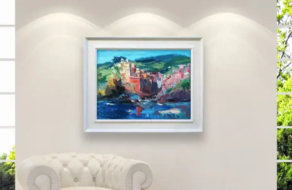The horizontal Riomaggiore seaside painting displayed inside an elegant white frame above a luxury white leather armchair.