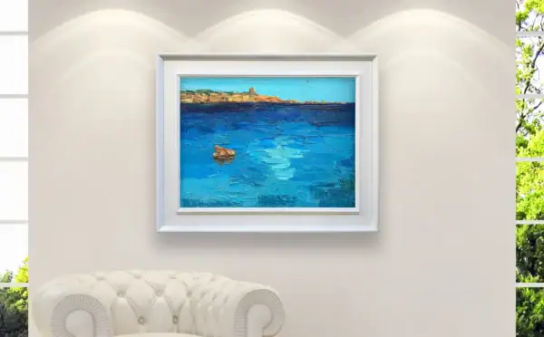 The horizontal Sardinia seascape oil painting styled beautifully inside an elegant white frame above a luxury white leather sofa.