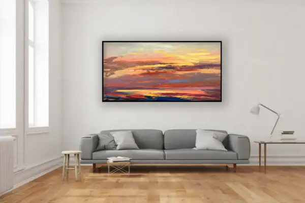 The large horizontal fiery sunset ocean canvas beautifully displayed on a white wall above a contemporary grey sofa.