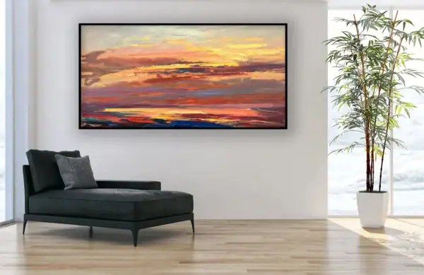 The horizontal vibrant coastal canvas hanging styled in a bright minimalist interior next to a black leather chaise longue and a tall potted plant.