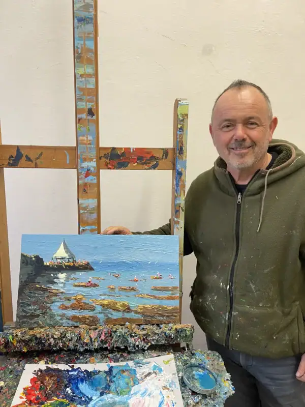 Italian painter Agostino Veroni standing in his fine art studio next to the original Livorno seascape oil painting displayed on the wooden easel.