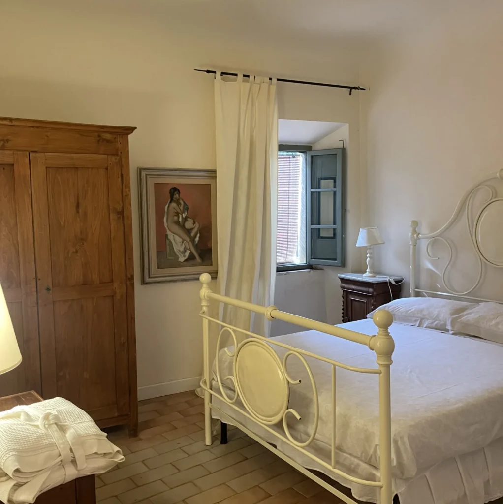 Traditional double bedroom with white wrought iron bed, historic decor, and fine art painting at Villa Minghetti Tuscan villa vacation rental.
