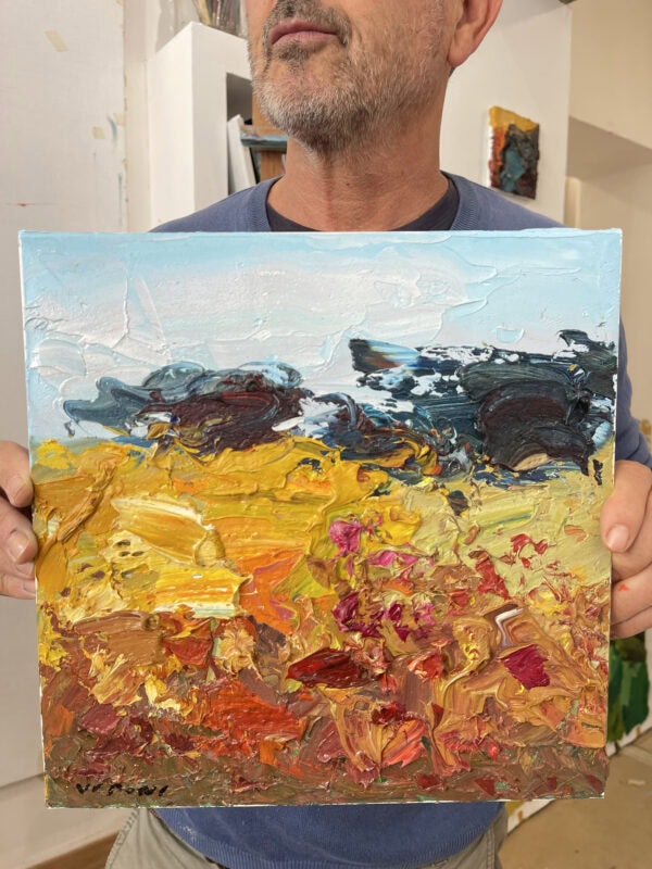 Abstract landscape oil painting on canvas held by artist Agostino Veroni in his studio. Showing scale of modern impasto artwork depicting a golden summer Tuscan field.