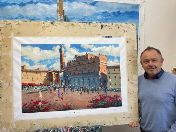 Artist Agostino Veroni standing next to his Siena oil painting on canvas. The textured painting depicts Piazza del Campo with Palazzo Pubblico and Torre del Mangia under a blue sky.