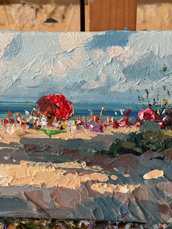 Summer beach oil painting on canvas detail on easel focusing on red beach umbrella. Rich impasto palette knife texture with vivid coastal colors, sand, and blue horizon.
